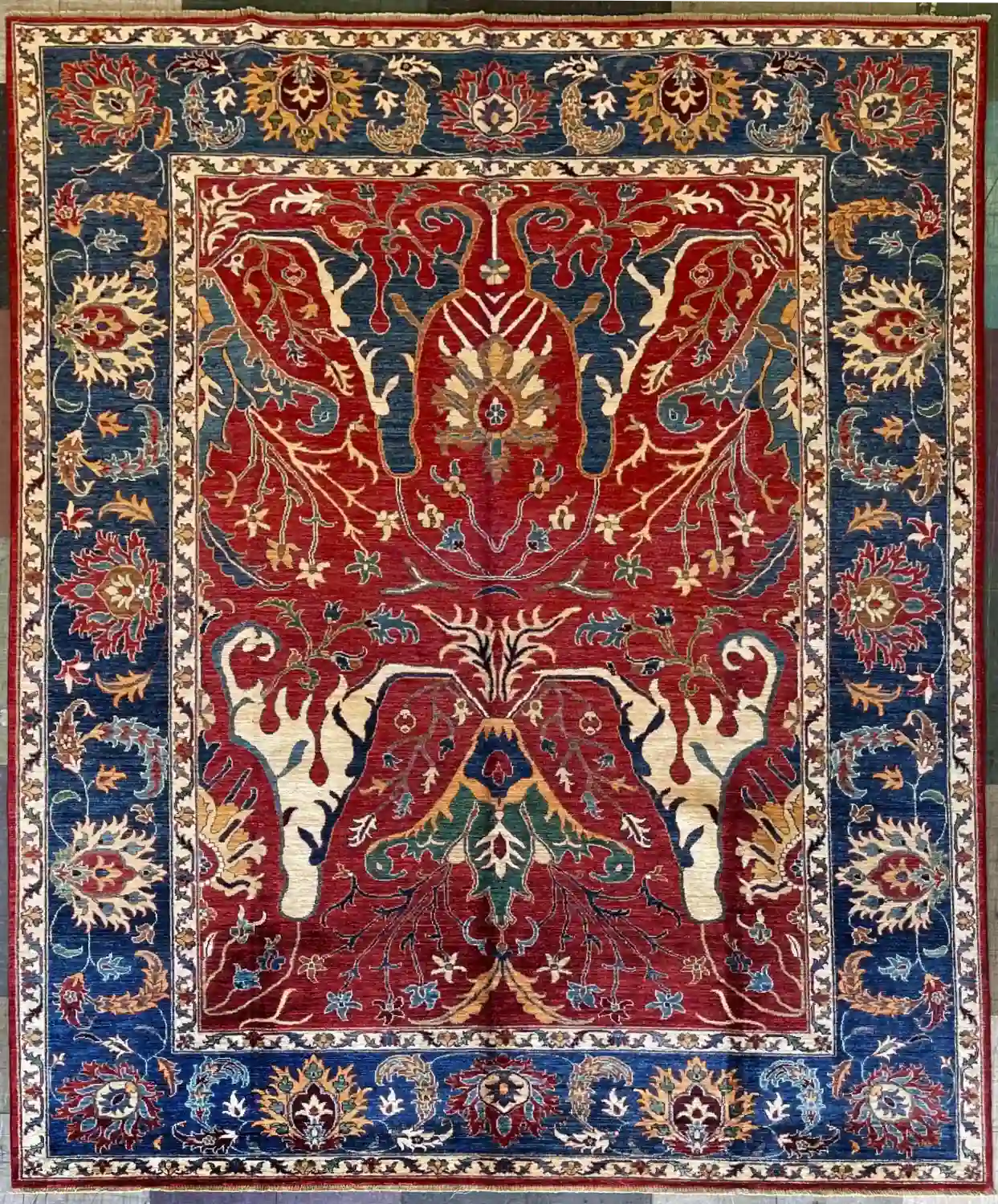 hand-knotted-chobi-wool-area-rug-7-11-x-10-2-ruby-red-prussian-blue-sku-112525-11.webp | McFarlands Carpet and Rug Service Ruby red hand-knotted Chobi wool area rug 7.11' x 10.2' with a mirror-image Tree of Life layout and a thick Prussian blue border.