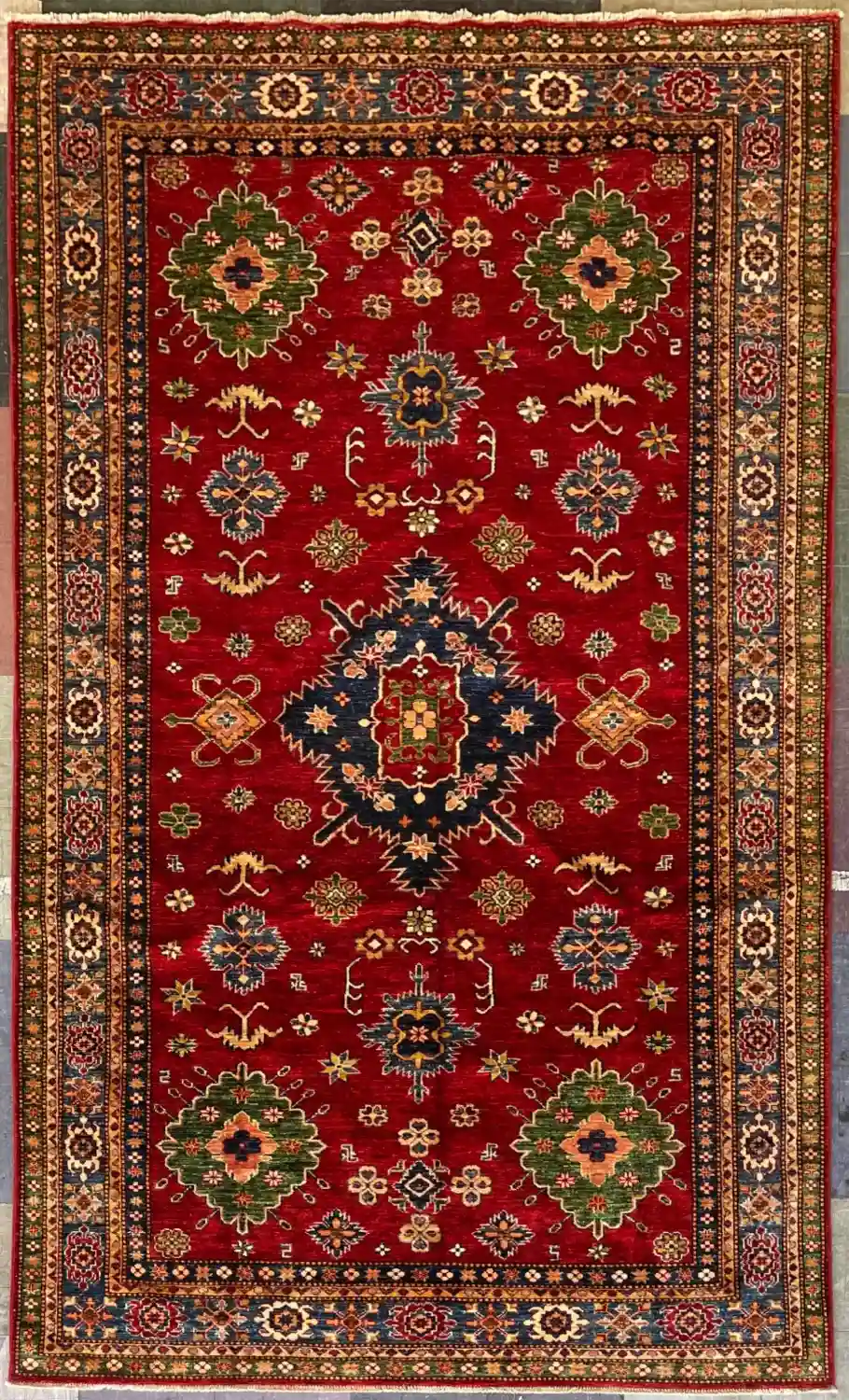 traditional-red-kazak-medallion-rug-6x10.webp | McFarlands Carpet and Rug Service Traditional red Kazak hand-knotted wool area rug 6.1' x 10.3' featuring a large geometric navy center medallion and green corners.