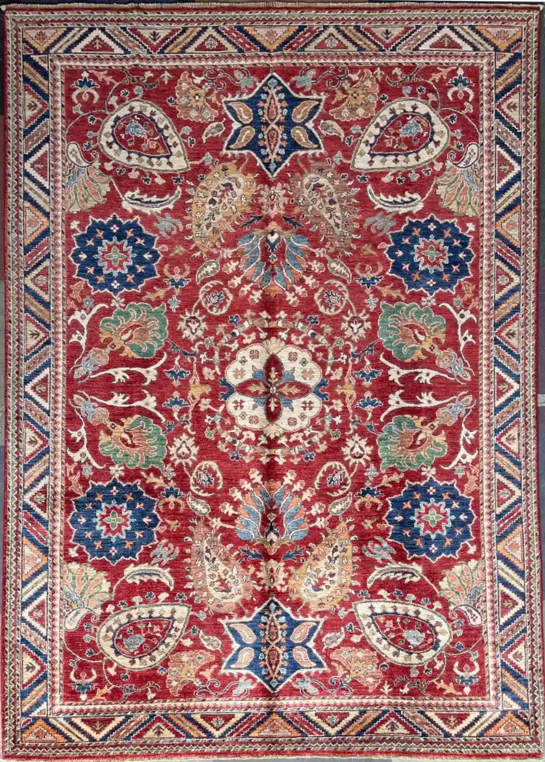 crimson-red-chobi-wool-area-rug-6x9.webp | McFarlands Carpet and Rug Service Hand-knotted Chobi wool area rug 6.2' x 9' with crimson red field, floral medallions, and a geometric chevron border.