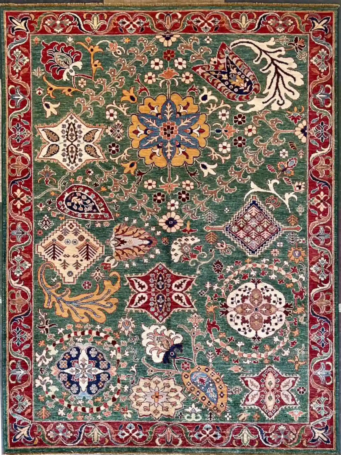 traditional-green-chobi-peshawar-floral-wool-rug-5x7.webp | McFarlands Carpet and Rug Service Traditional green Chobi Peshawar hand-knotted wool area rug 5.8' x 7.3' featuring multi-colored floral palmettes and a deep red border frame.
