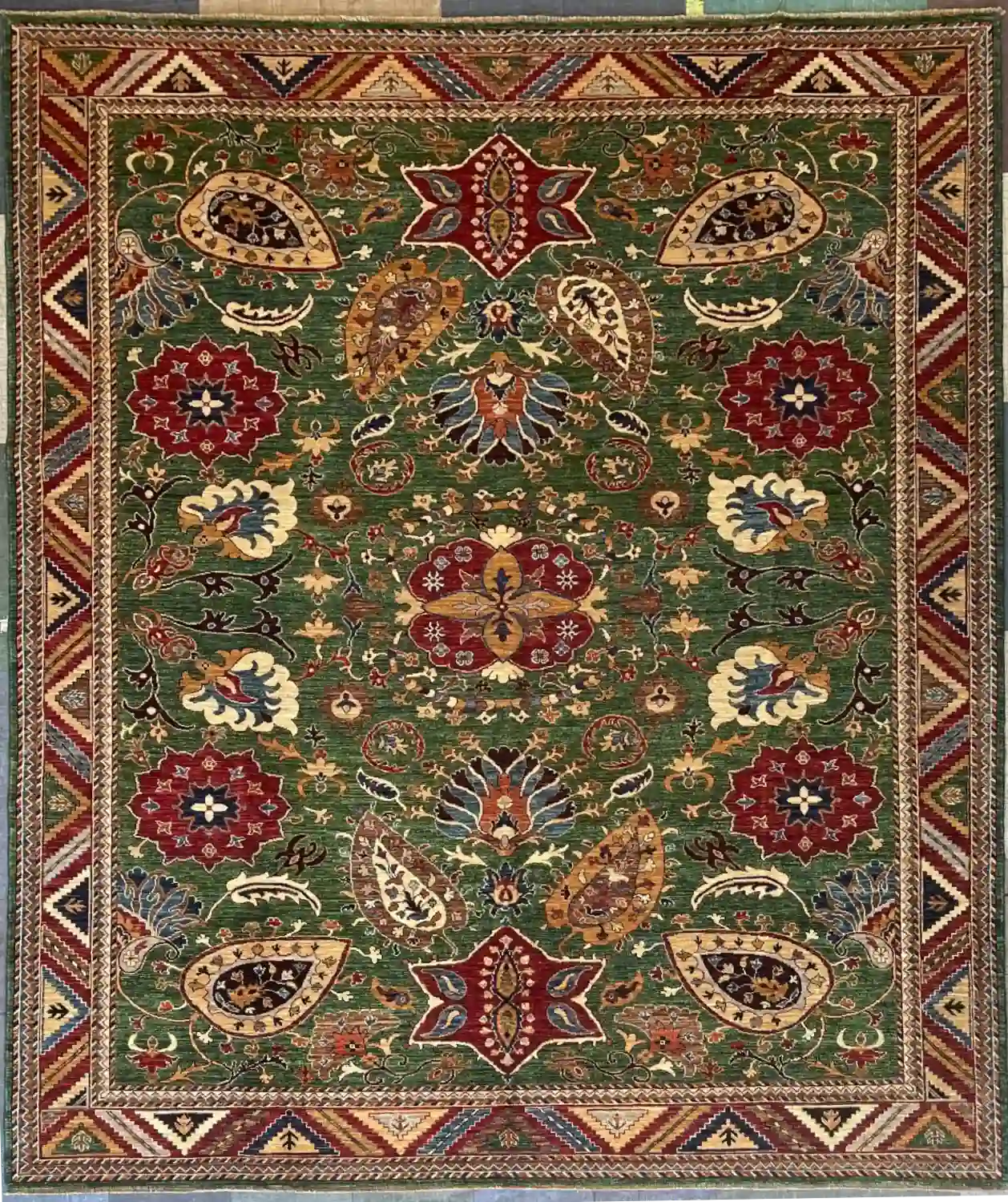 hand-knotted-chobi-wool-area-rug-8-4-x-10-3-green-sku-112525-5.webp | McFarlands Carpet and Rug Service Green Hand-Knotted Chobi Wool Area Rug 8.4' x 10.3' with red floral medallions and a geometric chevron border.