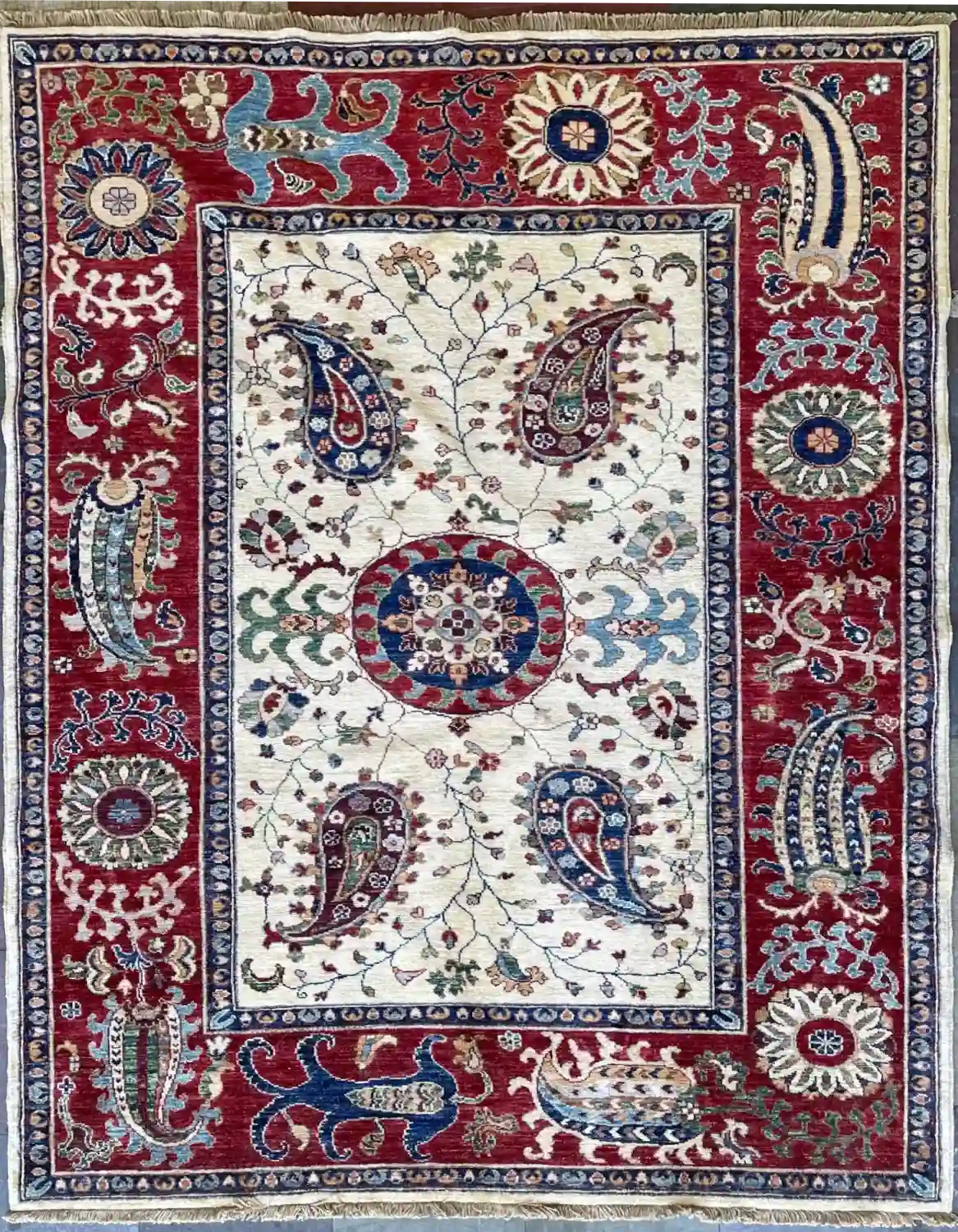 ivory-chobi-peshawar-paisley-wool-rug-5x7.webp | McFarlands Carpet and Rug Service Traditional ivory Chobi Peshawar hand-knotted wool area rug 5' x 6.6' featuring navy blue paisley motifs and a bold crimson red border frame.