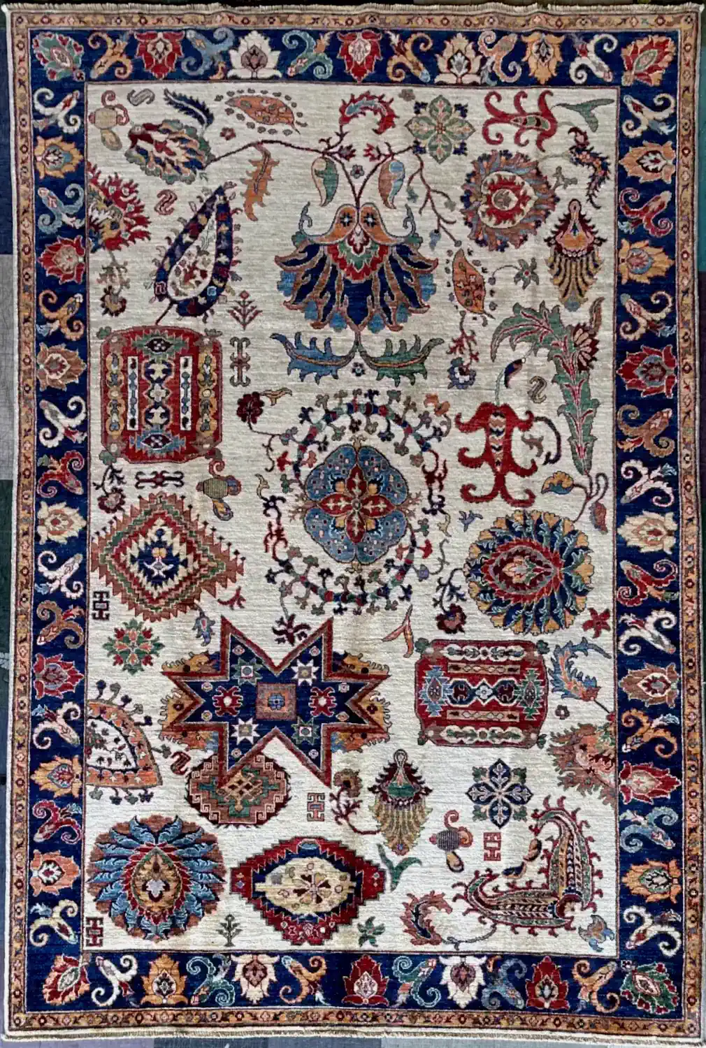 ivory-cobalt-blue-tribal-sampler-chobi-peshawar-wool-area-rug-6x9.webp | McFarlands Carpet and Rug Service Hand-knotted Chobi Peshawar wool area rug 6.4' x 9.0' with ivory field, tribal sampler motifs, geometric star emblem, and cobalt blue border.