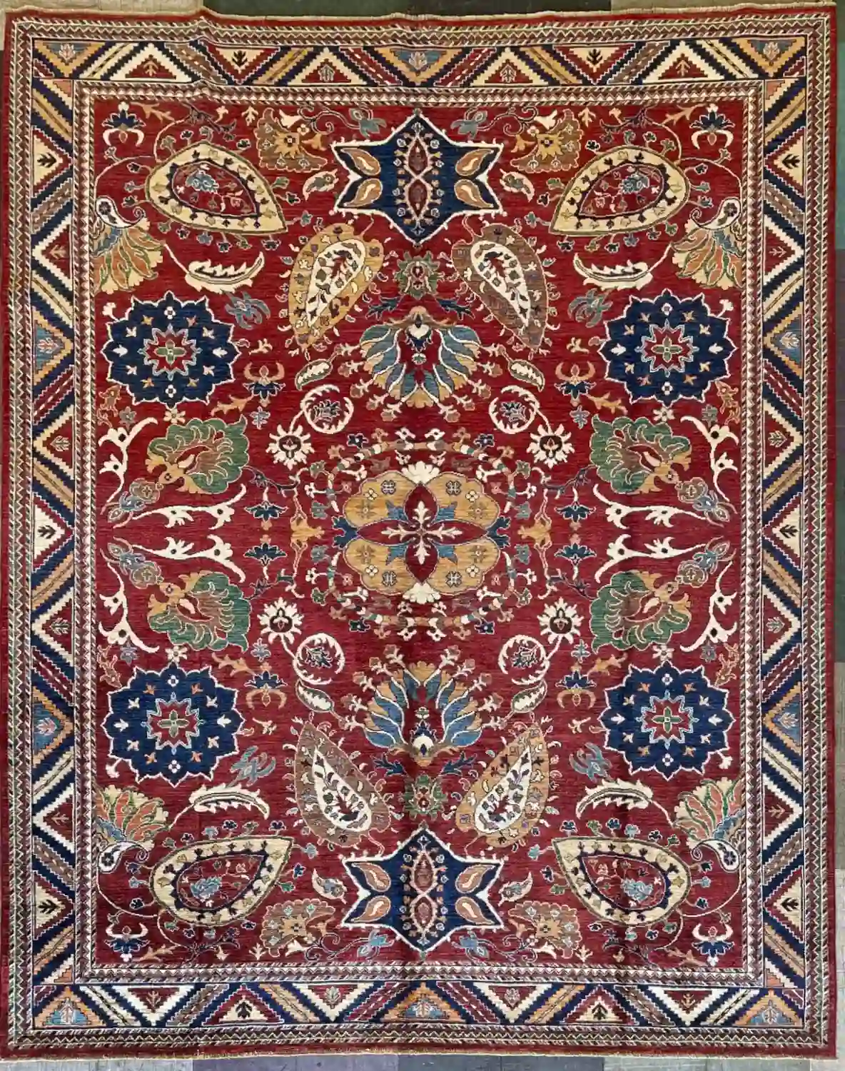 hand-knotted-chobi-wool-area-rug-8-2-x-10-1-crimson-red-sku-112525-9.webp | McFarlands Carpet and Rug Service Symmetrical red hand-knotted Chobi wool area rug 8.2' x 10.1' featuring navy rosettes and a geometric zig-zag border.